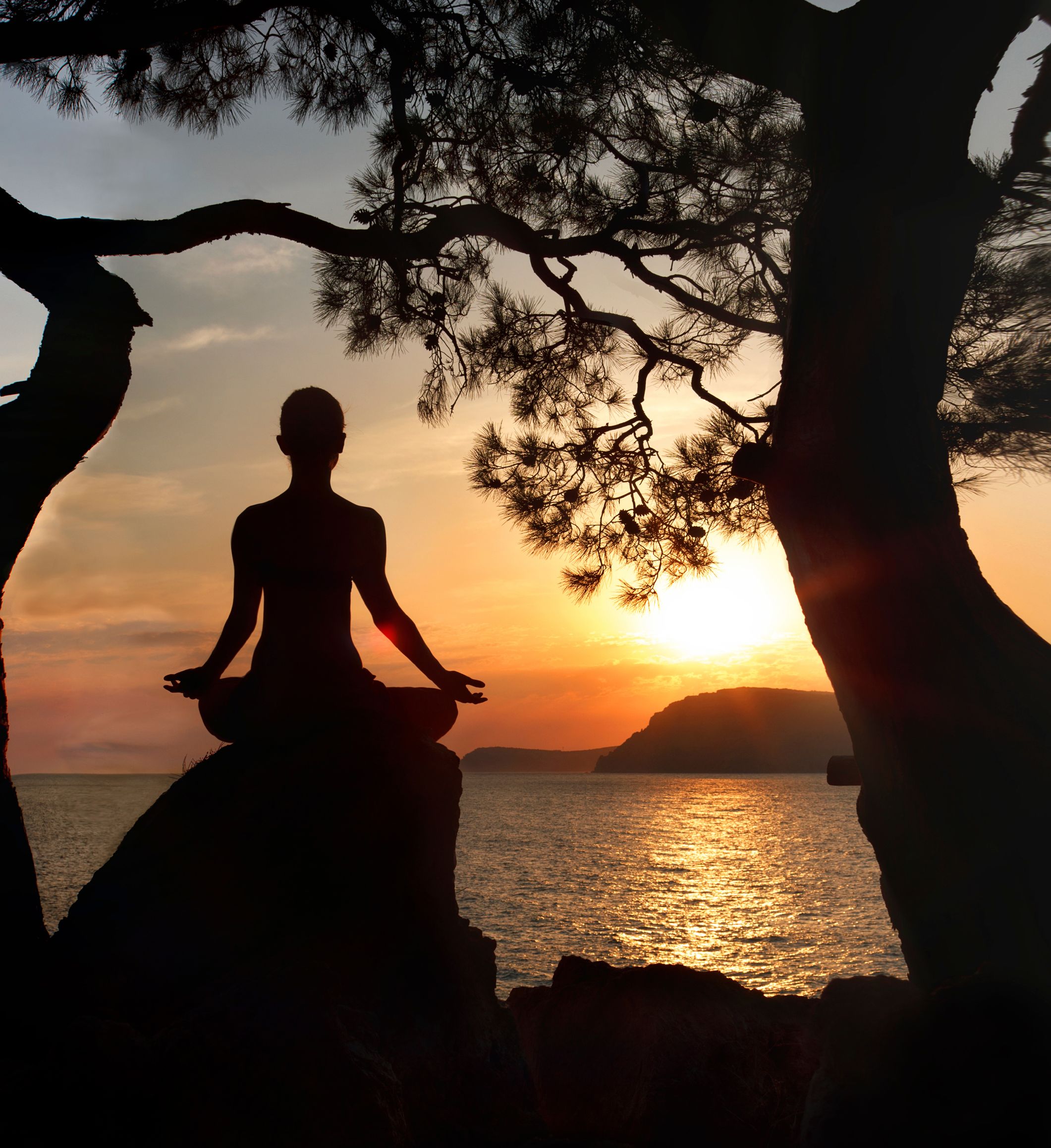 Woman sitting on a rock meditating at sunset