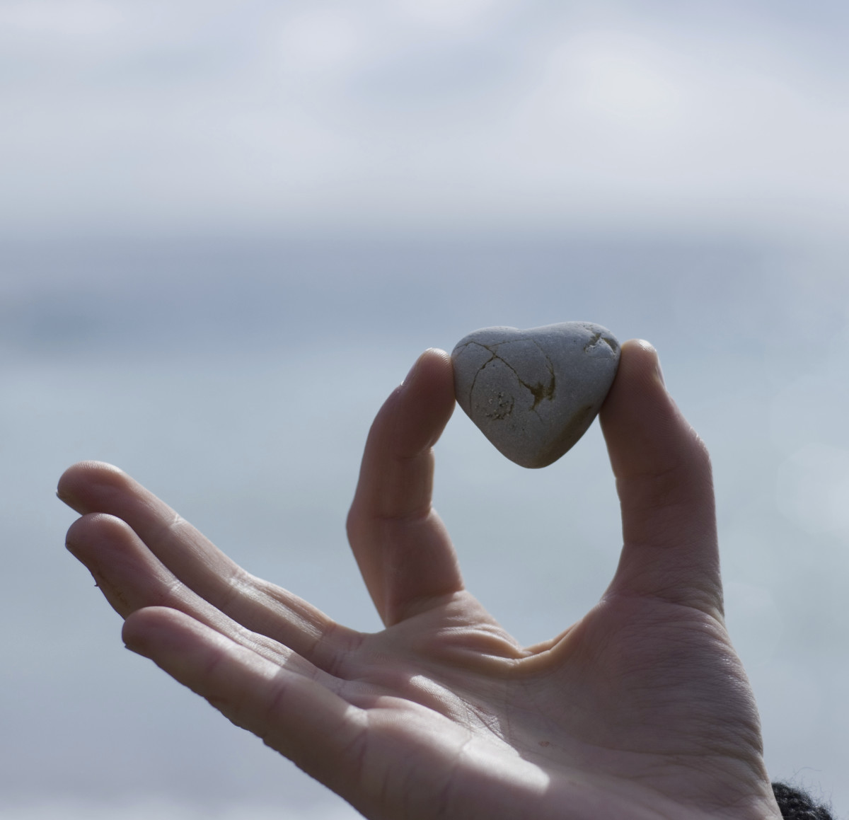 A hand holding a heart shaped rock between 2 fingers