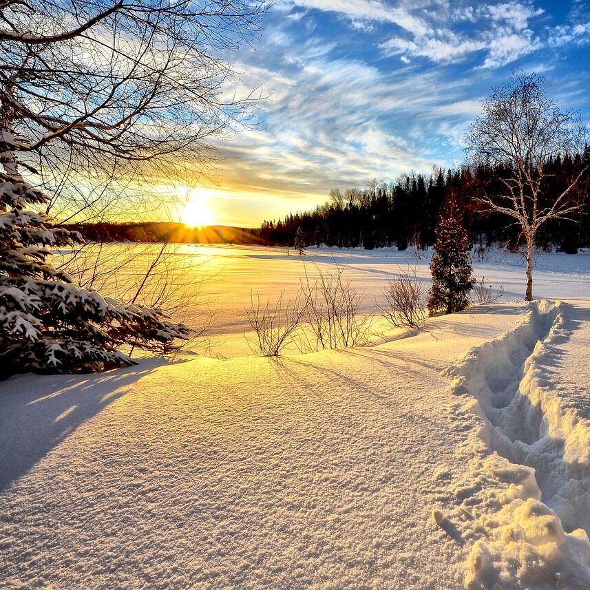 A view over a frozen, snow covered lake. Sun rising in the distance.